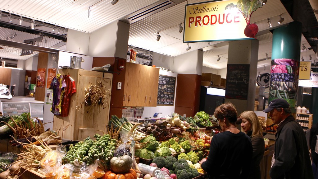 At Stillman’s produce stand, adjacent to Stillman’s meat stand, a vendor, left, guides two customers. Photo by Rebecce Jahnke.