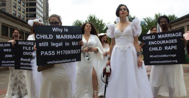 Activists in wedding gowns standing in front of the Statehouse