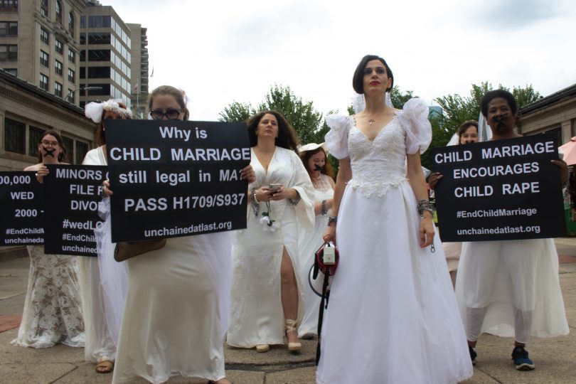Activists in wedding gowns standing in front of the Statehouse